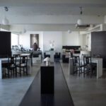 Sanctuary Mapo cafe interior in a minimalist black-and-white palette with concrete ceilings, white tables, cross-back chairs, globe lights, and curated shelves.